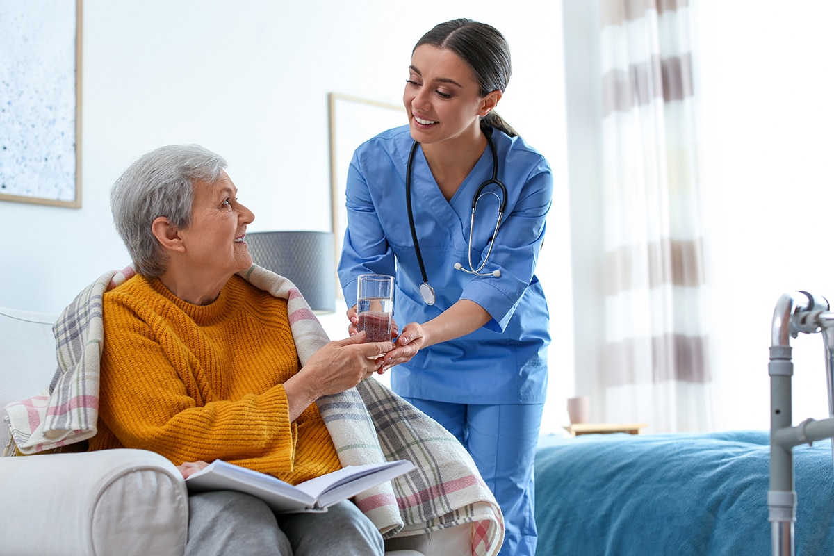Care worker giving water to elderly woman in geriatric hospice